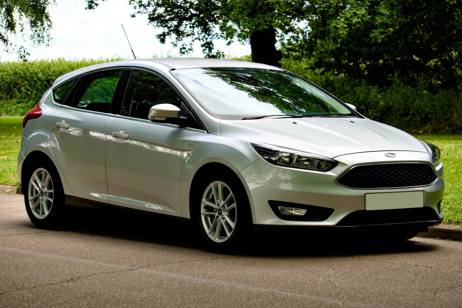 A sleek silver Ford Focus hatchback parked on a sunny day, with a scenic green background.