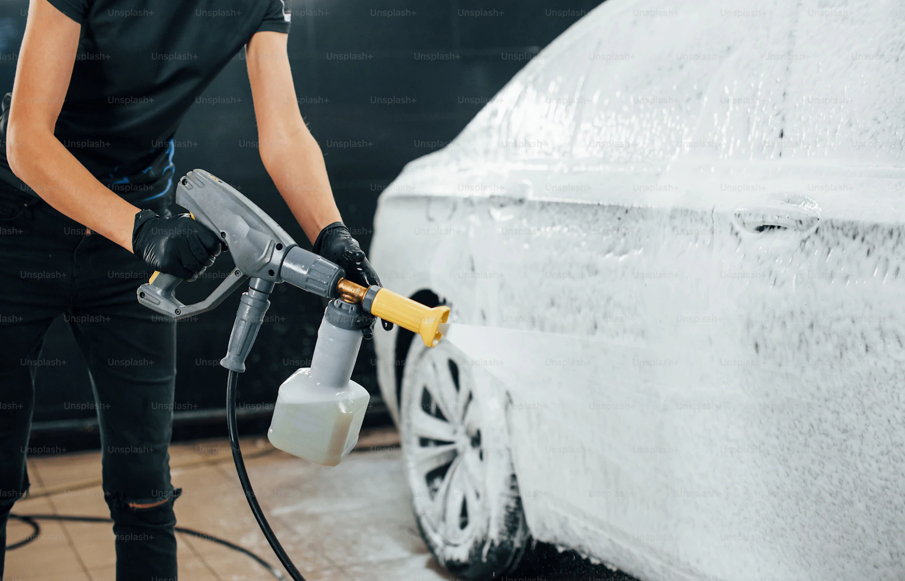 High pressure water cleaning a black car inside a car wash station