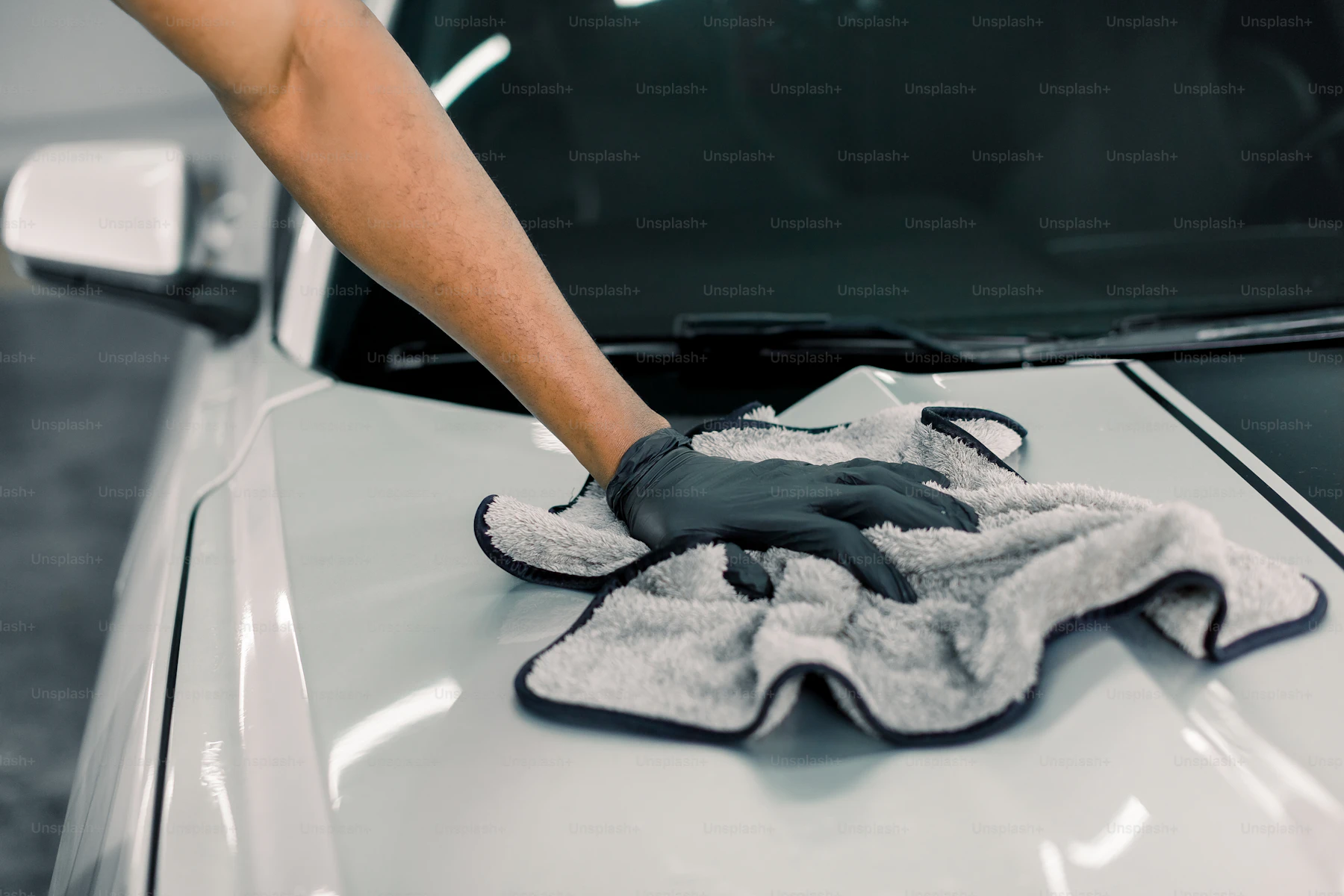 A gloved hand wiping the bonnet of a white car with a microfibre cloth